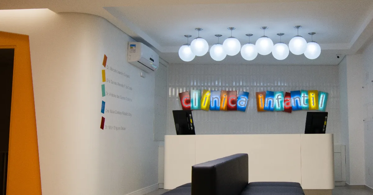 Recepção da Clínica Infantil: balcão branco, letreiro colorido iluminado e luminárias em globo